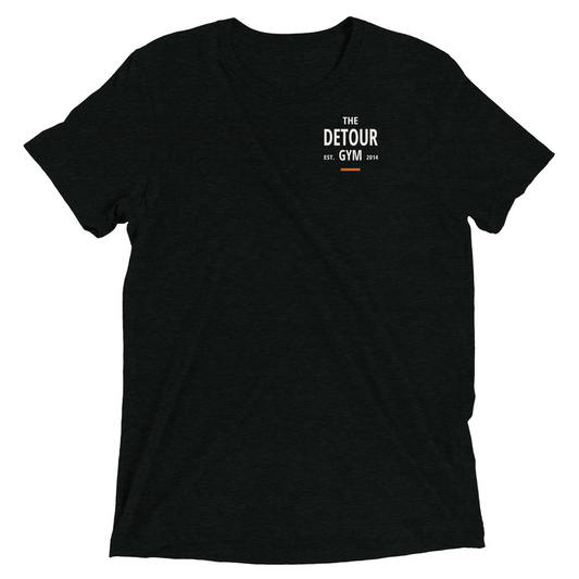 Foundation Everyday Tee in Solid Black Triblend, with enlarged left-chest Detour logo at the lower placement. Genuine Printful mockup.